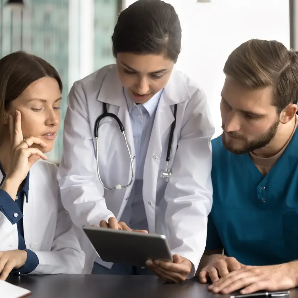 doctors examining information on tablet, at meeting in clinic led by Indian GP, explaining new apps, showing patient data, analyzing medical images such as x-rays or scans, discussing treatment plans