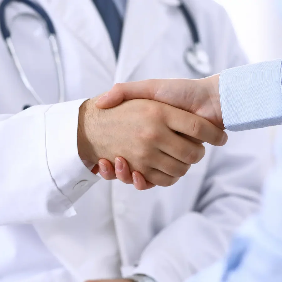Male doctor and woman patient shaking hands. Partnership in medicine, trust and medical ethics concept.